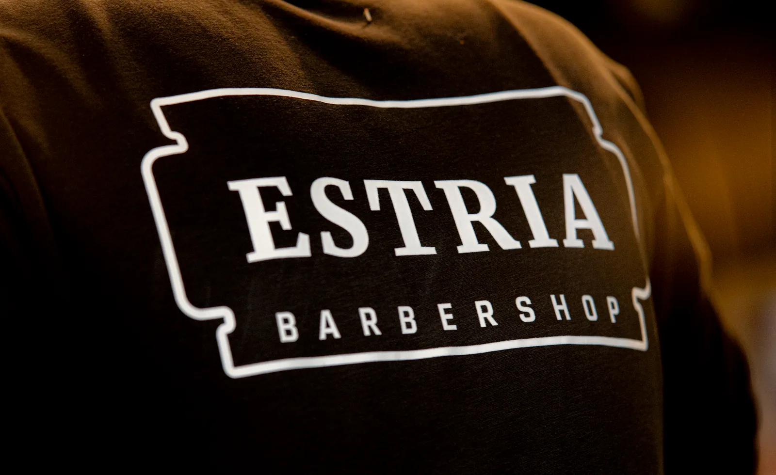 Het logo van Estria Barbershop op de trui van een barber